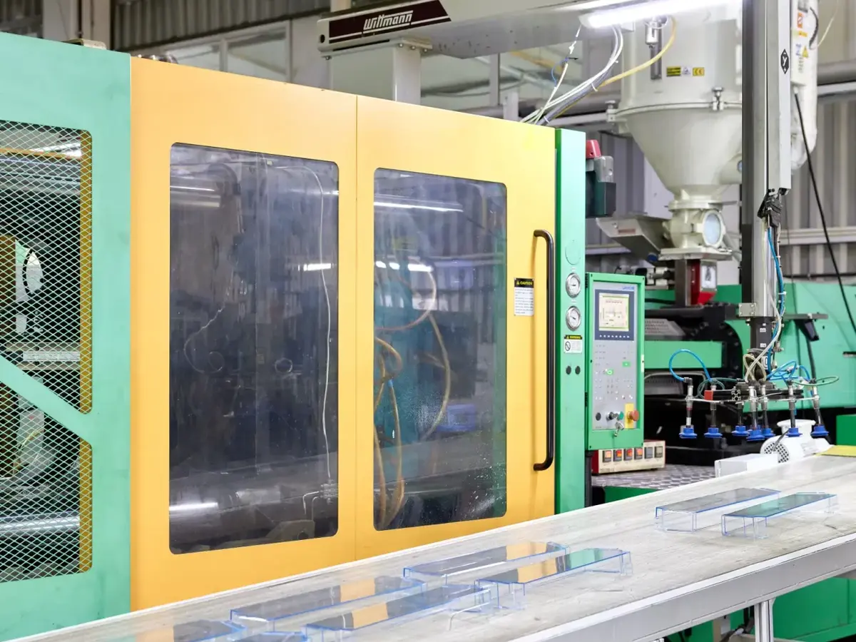 Injection molding machine producing clear plastic display components on a conveyor at the Surtas-USA factory