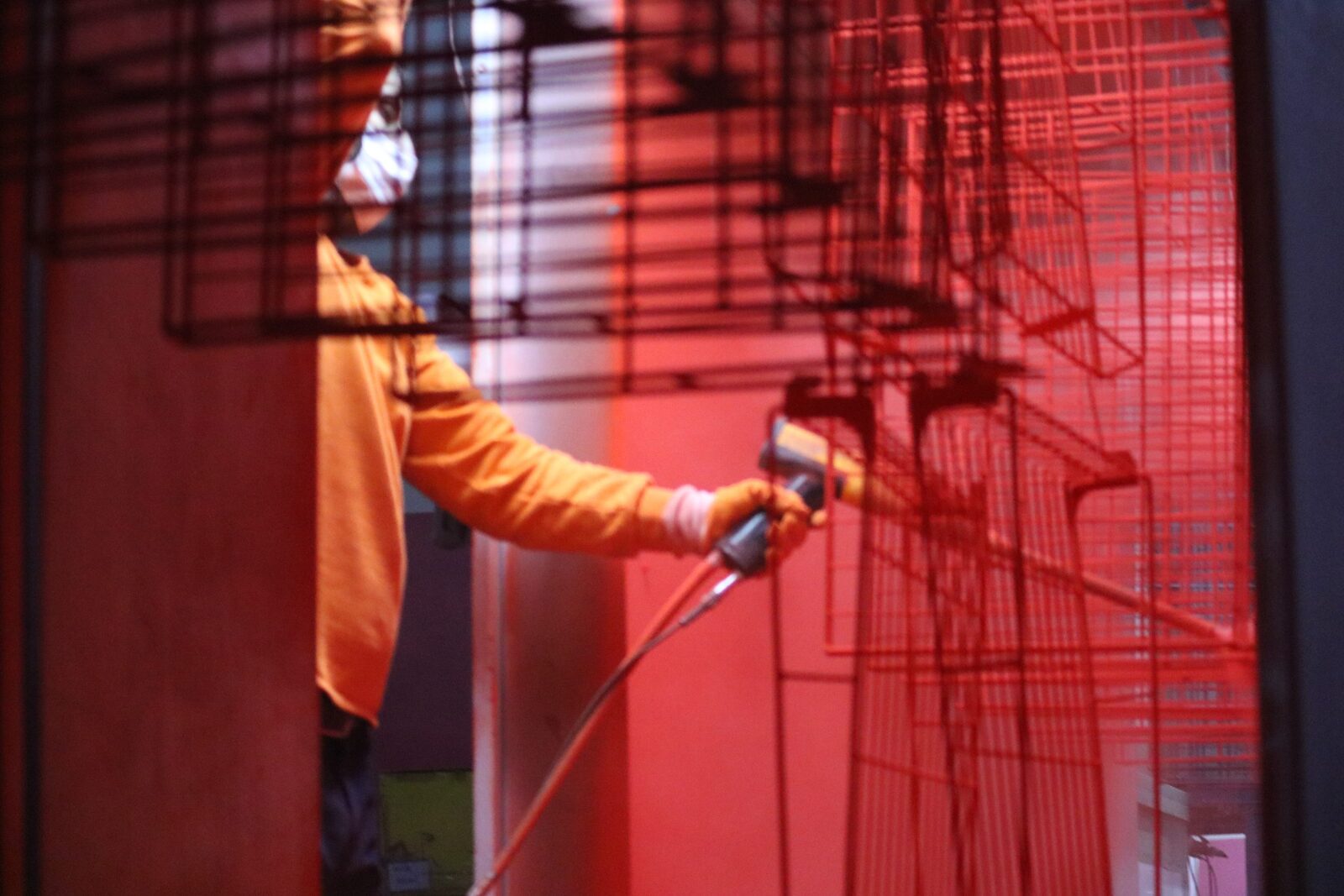 Worker in an orange suit powder coating a red wire display fixture