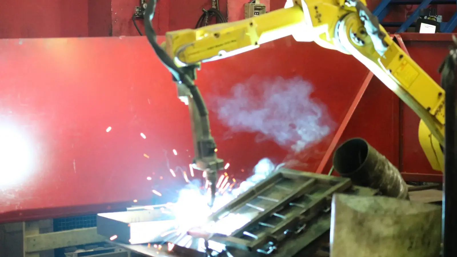 Yellow robotic welding arm welding a wire display frame, sparks visible