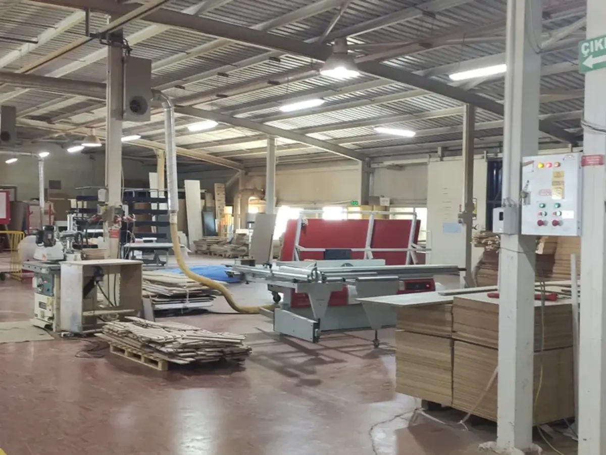 Woodworking shop floor with a panel saw, stacked wood panels, and cutting machinery at the Surtas-USA factory