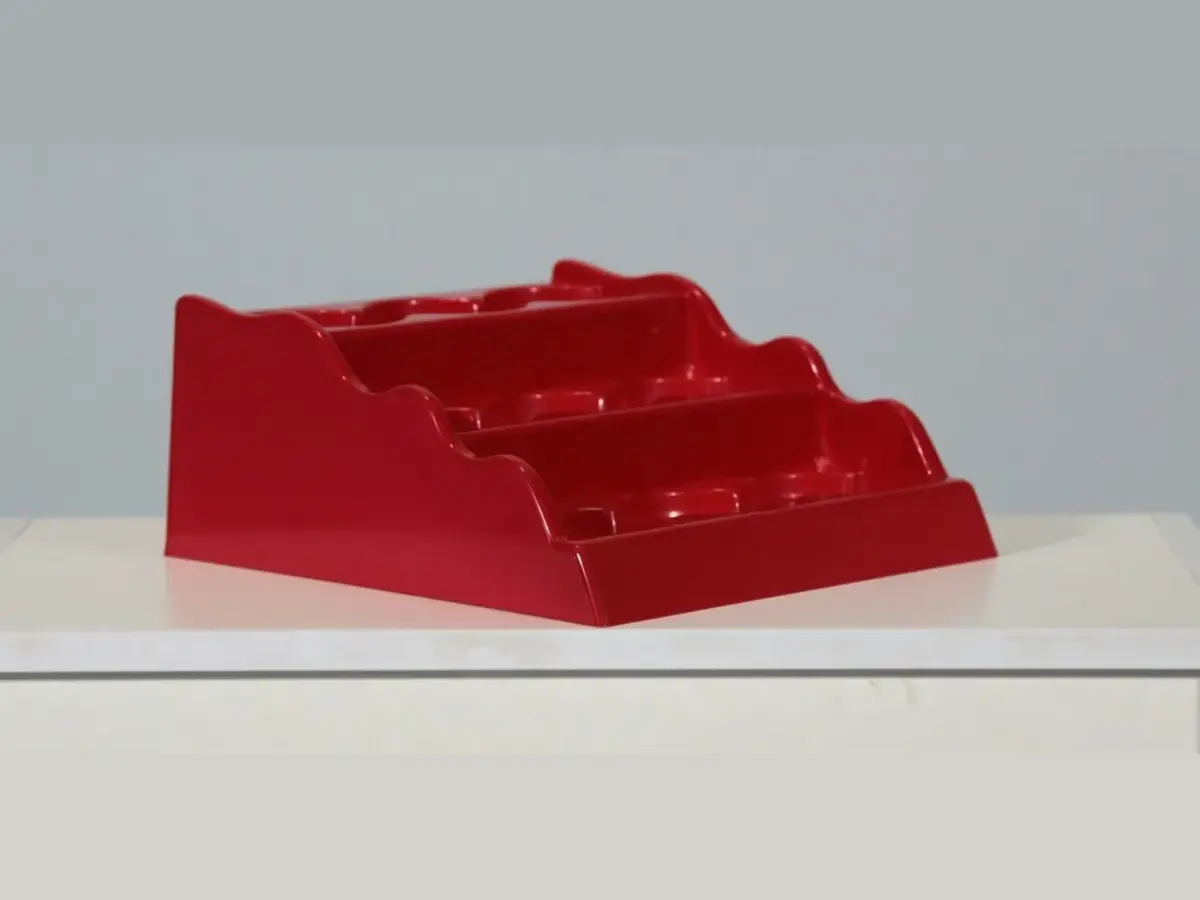 Red four-tier injection-molded countertop PDQ display tray shown empty on a white counter
