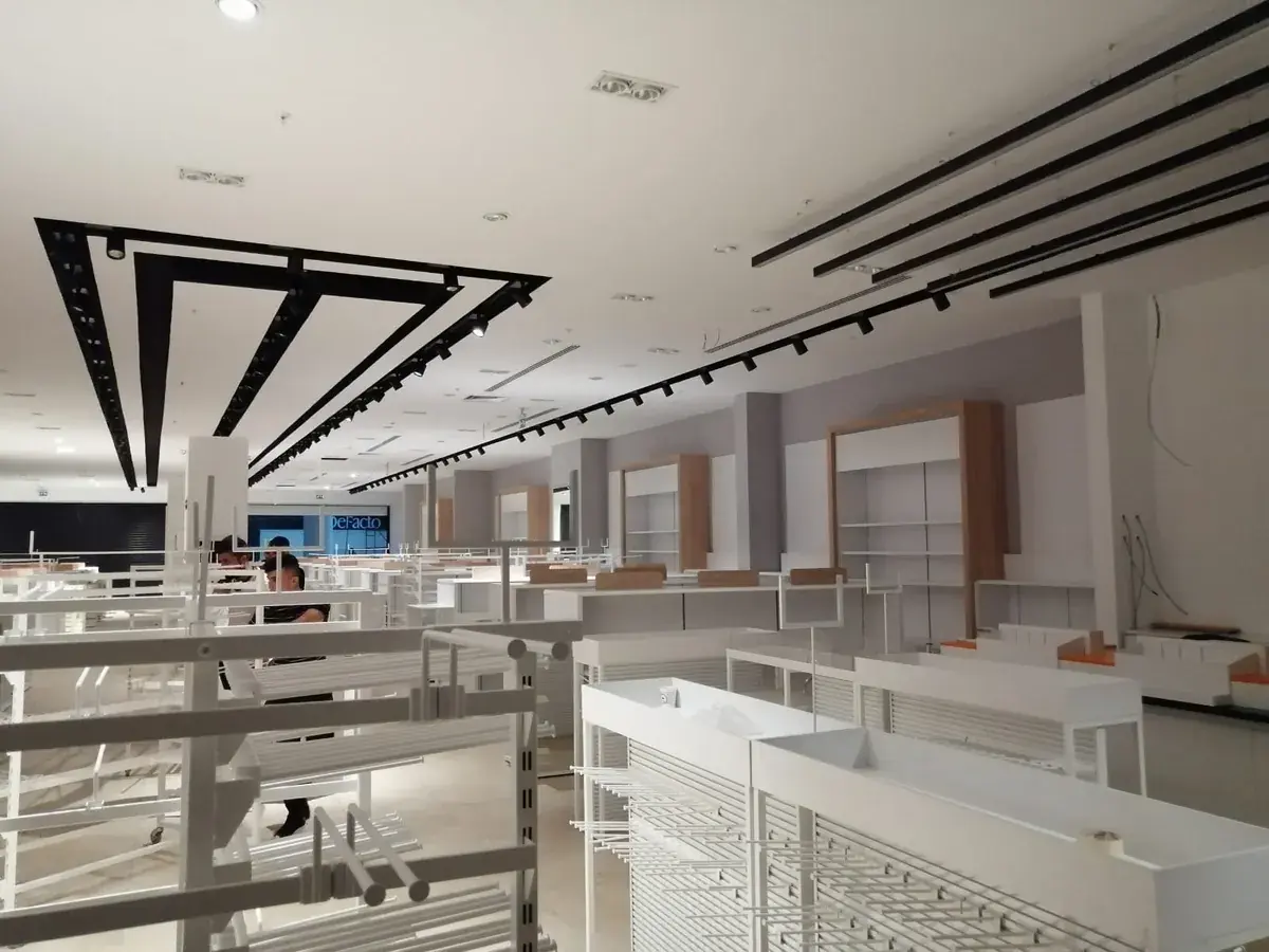 In-progress shop-in-shop retail fit-out with wood-accented wall fixtures, overhead track lighting installation, and clothing display racks